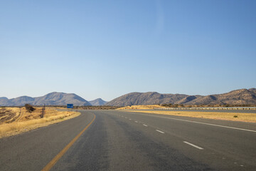 View of the open road between Windhoek and Outjo, surrounded by dry grasslands and distant mountains under a clear blue sky.