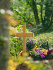 Holzkreuz ohne Namen am Grab mit Blumen