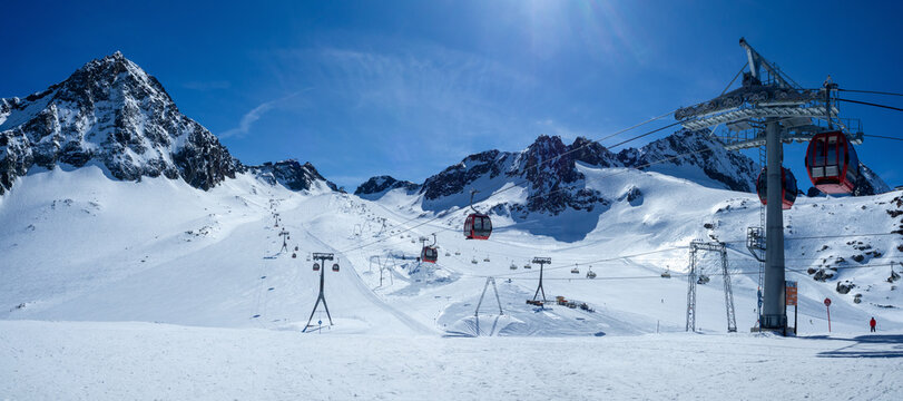 Stubai glacier in Austrian Alps with ski slopes, cable car gondolas, chairlift with skiers and snowboarders and a ski tow. Schaufelspitze summit in the background