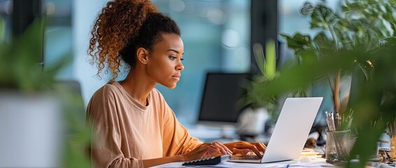 Focused young African American businesswoman working on laptop in modern office.