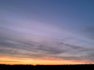 Beautiful colorful sunset sky with vibrant orange and purple clouds above dark forest silhouette