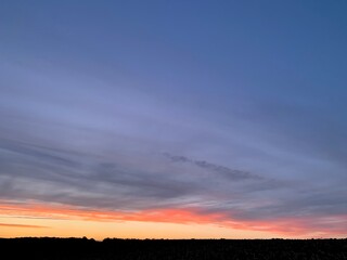 Beautiful colorful sunset sky with vibrant orange and purple clouds above dark forest silhouette