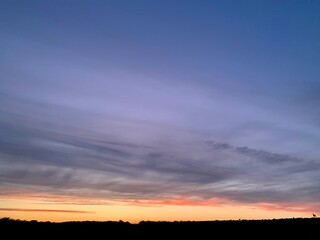 Fototapeta premium Beautiful colorful sunset sky with vibrant orange and purple clouds above dark forest silhouette