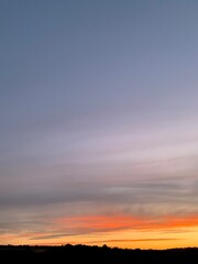 Beautiful colorful sunset sky with vibrant orange and purple clouds above dark forest silhouette