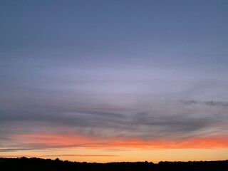 Beautiful colorful sunset sky with vibrant orange and purple clouds above dark forest silhouette