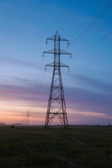 Tall electricity pylon standing in open field at twilight
