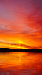 Naklejka premium Vibrant sunset over calm water reflecting fiery sky colors