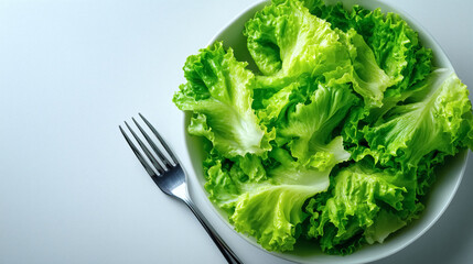 Fresh crisp lettuce leaves in a white bowl with a silver fork ready for a healthy meal