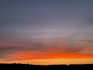 Beautiful colorful sunset sky with vibrant orange and purple clouds above dark forest silhouette