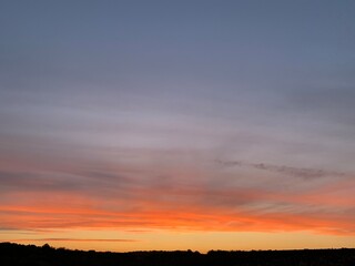 Beautiful colorful sunset sky with vibrant orange and purple clouds above dark forest silhouette