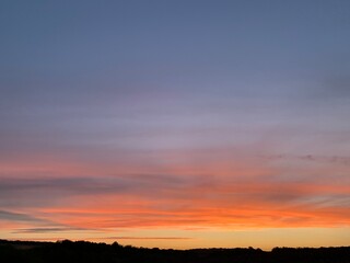 Beautiful colorful sunset sky with vibrant orange and purple clouds above dark forest silhouette