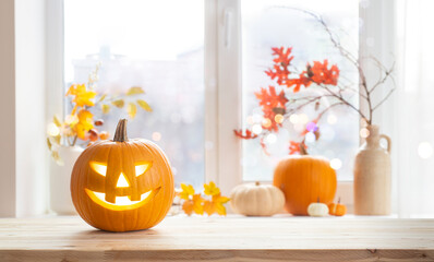 Orange jack o lantern pumpkin on wooden table with copy space over blurred window sill background...