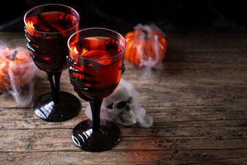 Halloween spooky red cocktail in skeleton hand glass on rustic wooden table. Copy space
