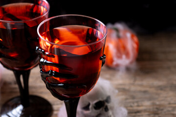 Halloween spooky red cocktail in skeleton hand glass on rustic wooden table. Copy space