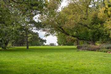A wide green lawn stretches under tall trees, with chairs placed for rest. The peaceful park view invites relaxation and quiet time in nature.
