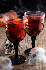 Halloween spooky red cocktail in skeleton hand glass on rustic wooden table