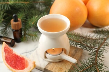 Aroma lamp with burning candle, grapefruits and fir tree branches on white table, closeup