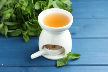 Aroma lamp with burning candle and mint leaves on light blue wooden table, closeup