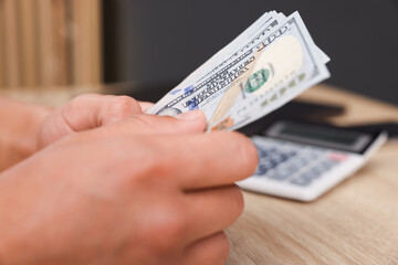 Man counting dollar banknotes at wooden table, closeup