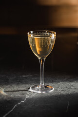Golden cocktail in elegant etched glass on dark stone background