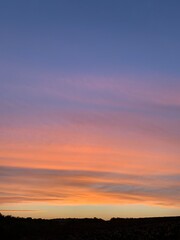 Beautiful colorful sunset sky with vibrant orange and purple clouds above dark forest silhouette