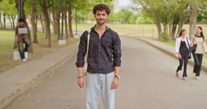 Indian happy young adult gen z proud male man look camera cross arm standing outdoor campus area. Cool pupil smart boy guy wear bag fold hand staring cam do casual pose enjoy new day garden place