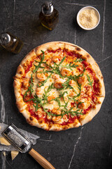 Shrimp and arugula pizza with cheese and tomato sauce on dark stone background