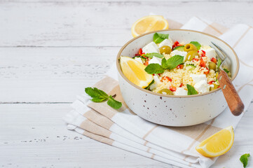 A bright, fresh salad with couscous, feta cheese, vegetables, and herbs on a light background. A healthy and delicious concept, a vegetarian dish for lunch or dinner.