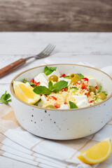 A bright, fresh salad with couscous, feta cheese, vegetables, and herbs on a light background. A healthy and delicious concept, a vegetarian dish for lunch or dinner.