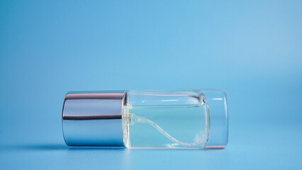 Glass cosmetic spray bottle with silver cap on blue background