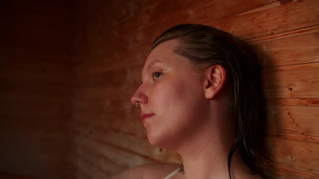 4K Handheld Close Up Shot of Beautiful Young Caucasian Woman in Warm Wooden Sauna, Relaxing and Meditating, Sweaty and Wet Hair and Skin, Spa Wellness and Mindfulness