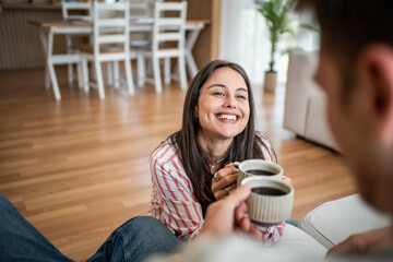 Happy couple sharing coffee at home on living room floor