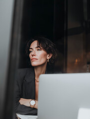Woman in blazer at laptop | Confident creative professional sitting at desk in moody lighting | Minimalist cinematic tone | Contemporary office portrait concept