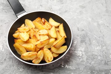 Tasty baked potatoes in frying pan on grey textured table, closeup. Space for text