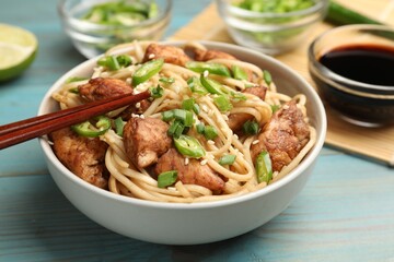 Tasty noodles with chicken, green peppers and sesame seeds served on blue wooden table, closeup