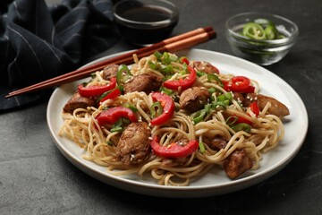 Tasty noodles with chicken, green onions and vegetables served on black table, closeup