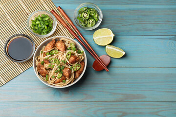 Tasty noodles with chicken, green peppers and sesame seeds served on blue wooden table, flat lay