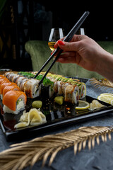 Philadelphia sushi set on a large black tray with soy sauce and a girl's hands with chopsticks