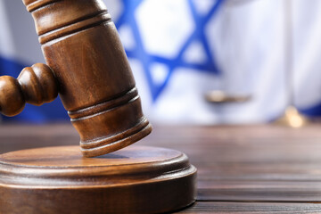 Judge's gavel on wooden table against flag of Israel, closeup. Space for text