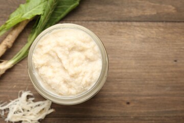 Tasty horseradish sauce and roots on wooden table, flat lay. Space for text