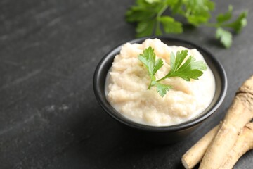 Tasty horseradish sauce with parsley and roots on black table, closeup. Space for text