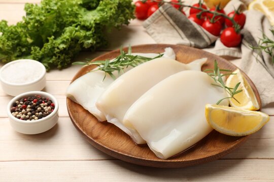 Pieces of raw squids with products and spices on light wooden table, closeup