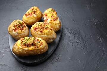 Tasty stuffed baked potatoes on black textured table, closeup. Space for text