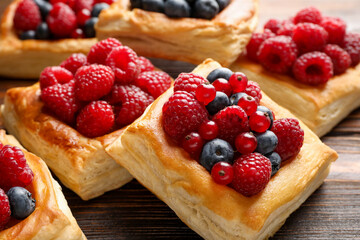 Tasty puff pastries with berries on wooden table, closeup