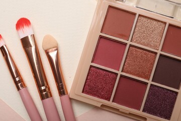 Colorful eyeshadow palette and makeup brushes on color background, flat lay