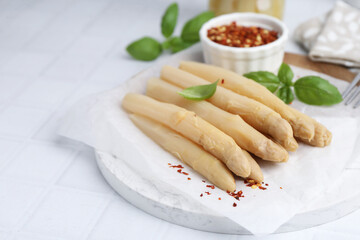 Pickled asparagus spears with spices and basil on white table, closeup