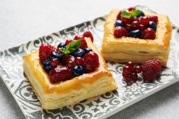 Tasty puff pastries with berries and mint on light grey table, closeup