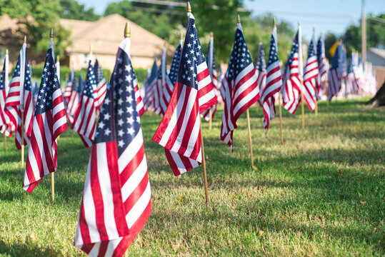 One flag stands in crisp focus against a softly blurred residential houses and neighborhood street, capturing the emotional clarity of remembrance in Texas patriotic 9/11 memorial landscape