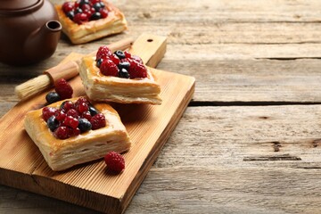 Tasty puff pastries with berries, teapot and brush on wooden table, closeup. Space for text
