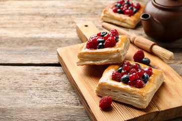 Tasty puff pastries with berries, teapot and brush on wooden table, closeup. Space for text